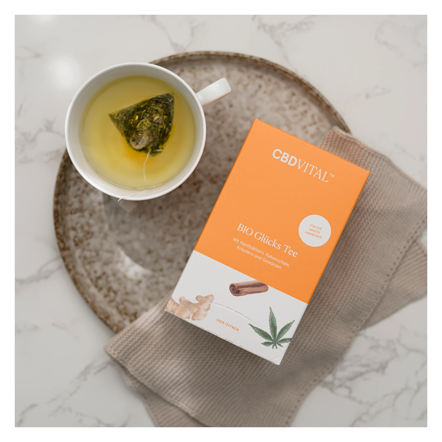 CBD VITAL Glücks Tee mit Hanfblättern – Teebeutel in weißer Tasse mit heißem Tee, daneben die Verpackung. Jetzt auf cbd-cannabidiol.de kaufen.